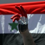 A Syrian protester makes a victory sign near their national flag during a protest calling for Syria's President Bashar al-Assad to step down, in front of the Syrian embassy in Amman