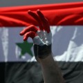 A Syrian protester makes a victory sign near their national flag during a protest calling for Syria's President Bashar al-Assad to step down, in front of the Syrian embassy in Amman