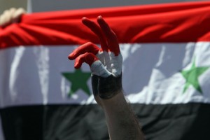 A Syrian protester makes a victory sign near their national flag