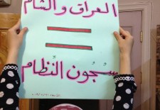 Suad holds up a placard that says "ISIS prisons= regime prisons." Photography by Zaina Erhaim.