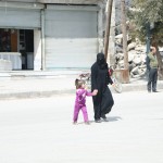سيدة وطفلتها تقطع الشارع أمام مبنى مهدم في حي المرجة في حلب. تصوير: حسام كويفاتية