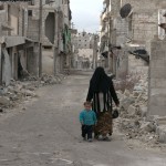 أمرأة تمشي مع طفلها في حارة مهدمة في السكري في حلب. تصوير براء الحلبي