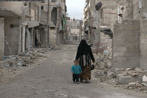 أمرأة تمشي مع طفلها في حارة مهدمة في السكري في حلب. تصوير براء الحلبي
