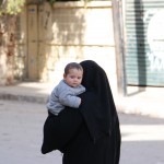 أمرأة تحمل رضيعها وتمشي في حي الزبدية. تصوير حسام كويفاتية