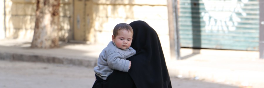 أمرأة تحمل رضيعها وتمشي في حي الزبدية. تصوير حسام كويفاتية