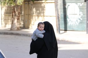 A woman carrying her child and walking in al-Zabdiah neighbourhood. Photo by: Baraa al-Halabi